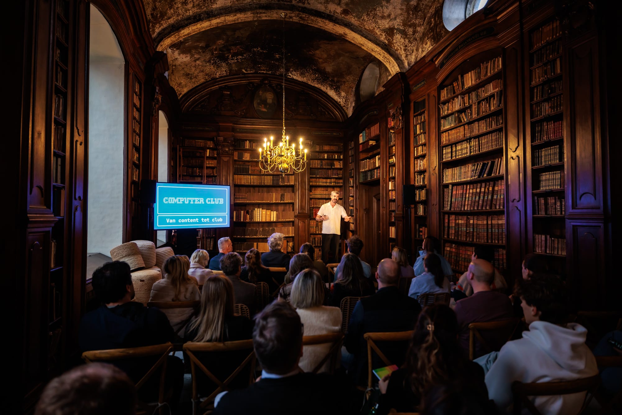 Een foto van een oude kloosterbibliotheek, waarin ik voor een publiek een slide presenteer met daarop het Computer Club-logo, en de titel: 'Van content to club.'